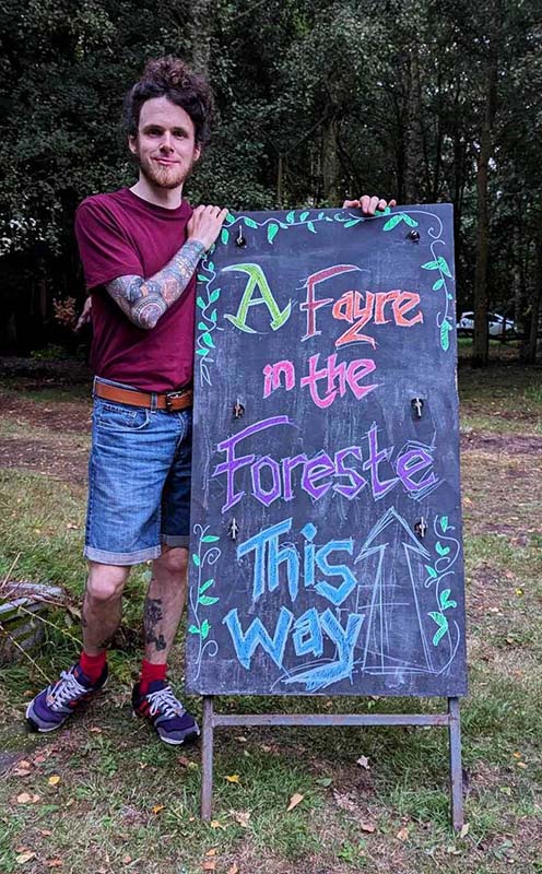 Groomsguard John holding a sign that reads 'Welcome to A Fayre in the Foreste'
